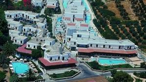 An aerial view of a coastal resort with multiple buildings, a swimming pool, and a beach area with clear waters.