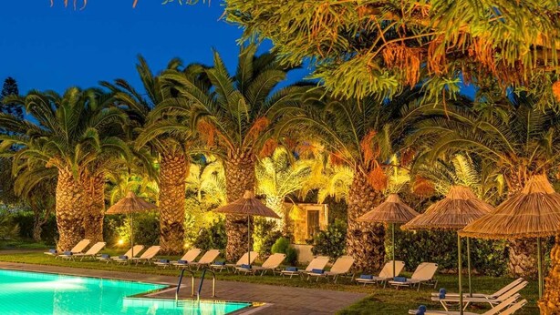 A poolside area with lounge chairs and palm trees, surrounded by a stone wall and a pool.