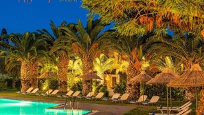 A poolside area with lounge chairs and palm trees, surrounded by a stone wall and a pool.