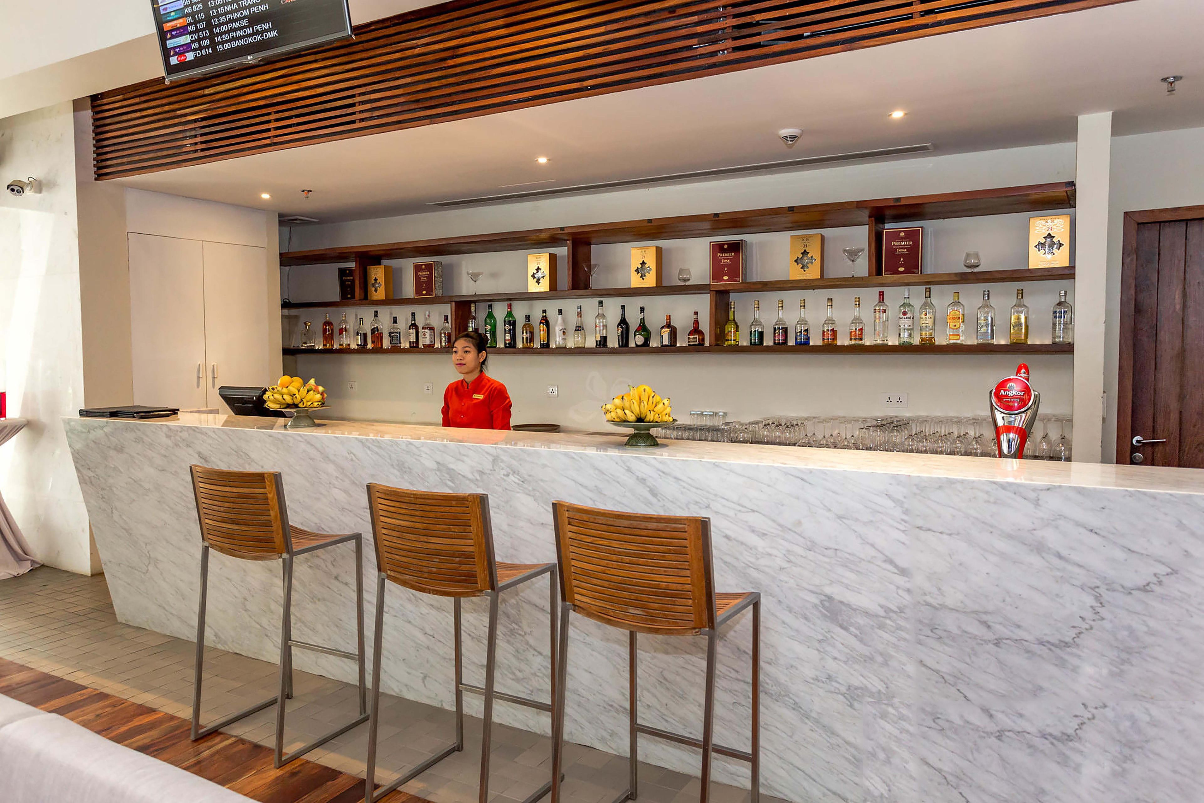A bar area with a marble counter, wooden chairs, and a variety of liquor bottles.