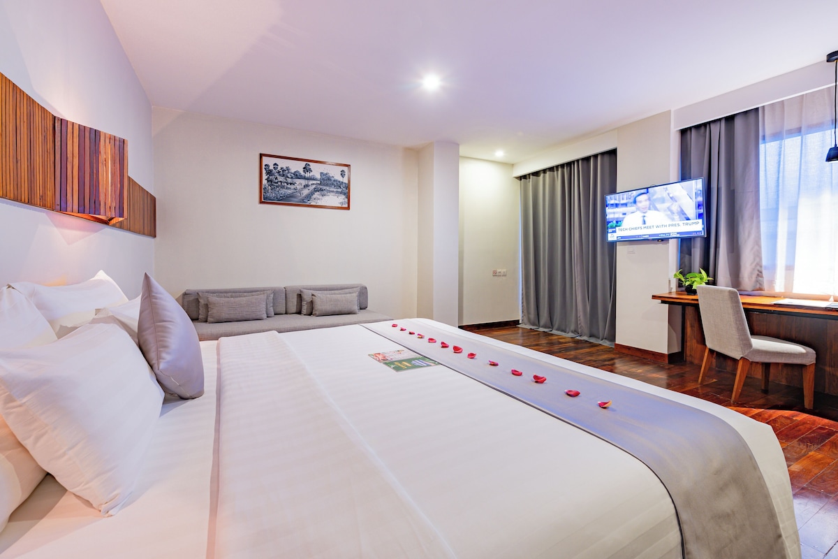 A hotel room with a large bed, a desk with a chair, a television, and a wall-mounted artwork.