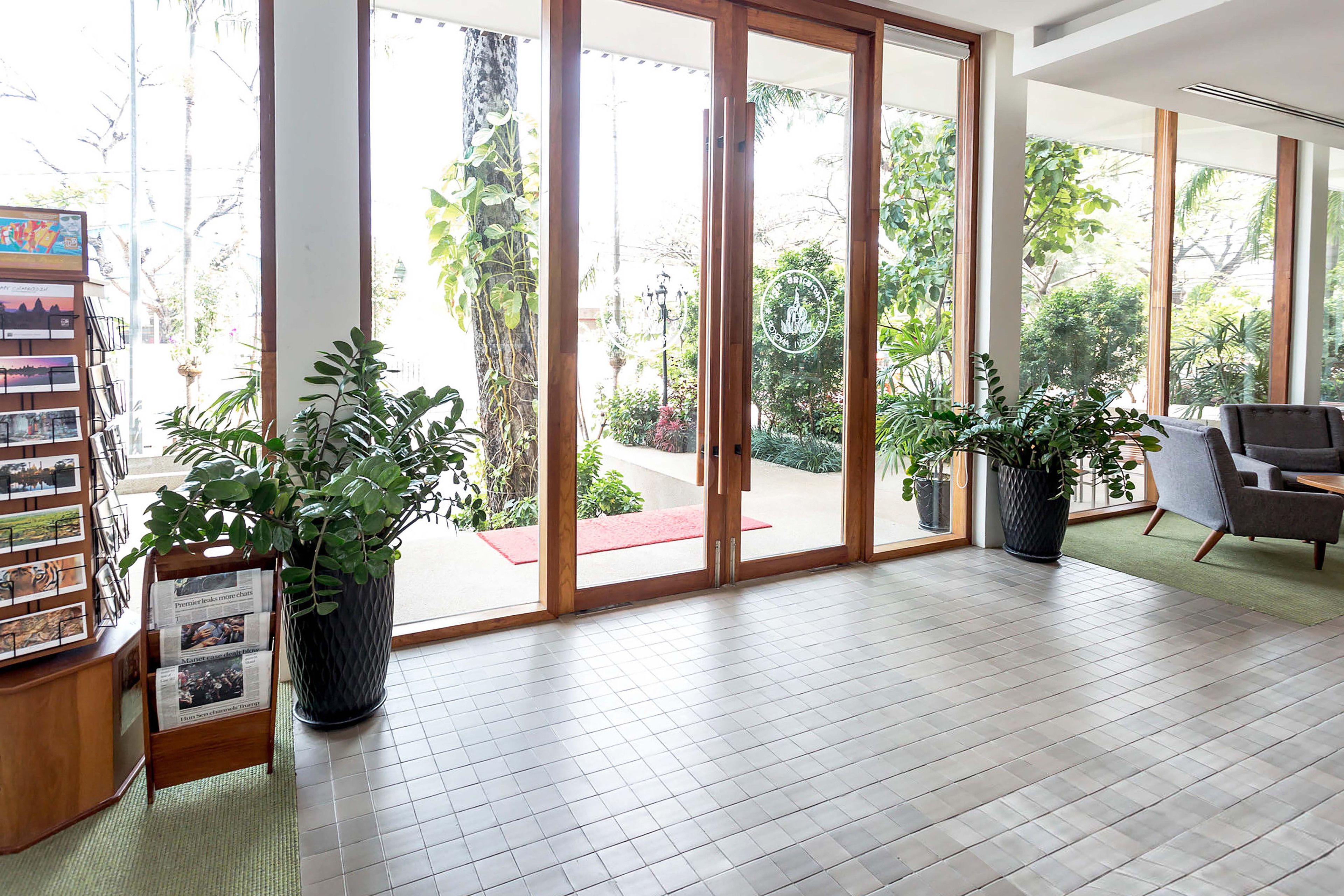 Amplia habitación con un gran ventanal corredero que da a un espacio exterior, un mostrador de recepción de madera y varias plantas en macetas.