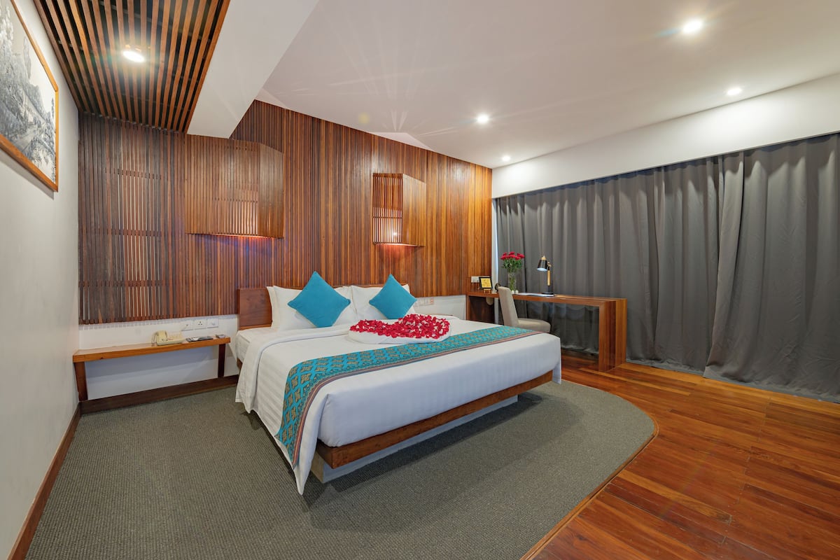 Een moderne hotelkamer met een groot bed, houten paneelwanden, een bureau met stoel en een groot raam met gordijnen.