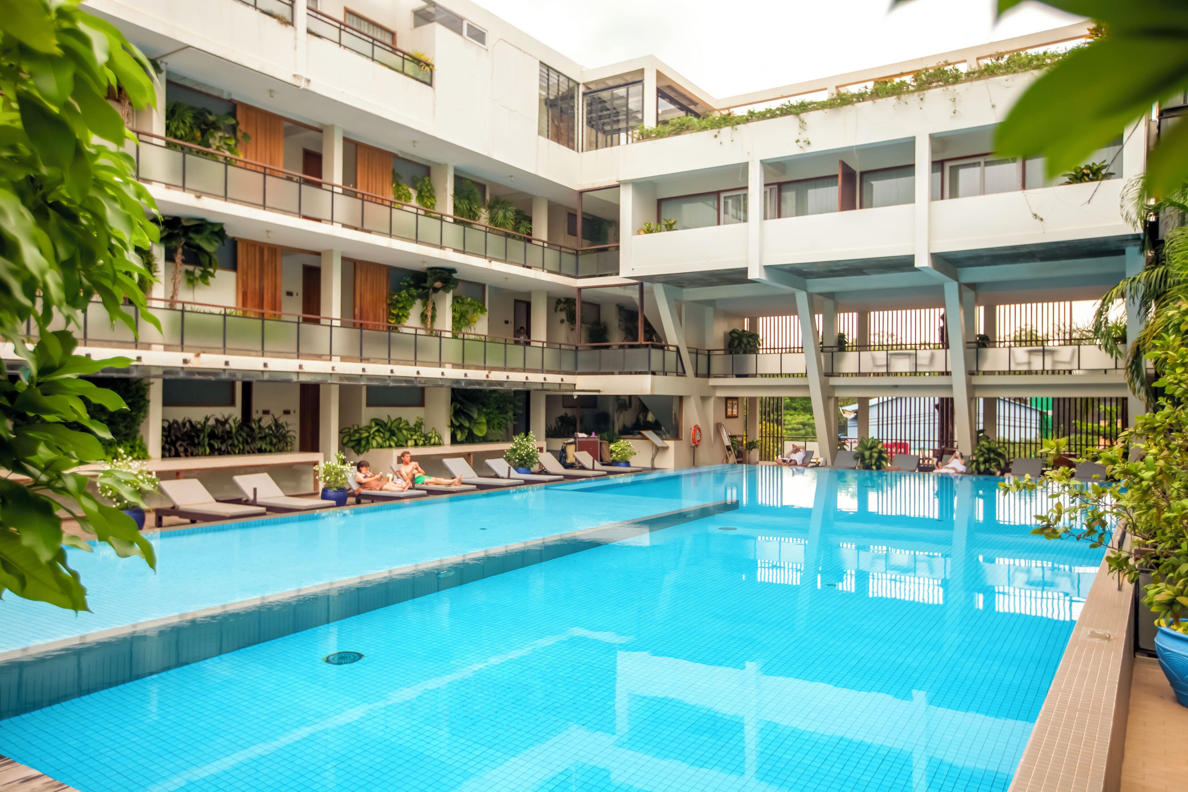 Una piscina interior de varios niveles, con múltiples balcones, sillones de descanso y plantas en macetas.