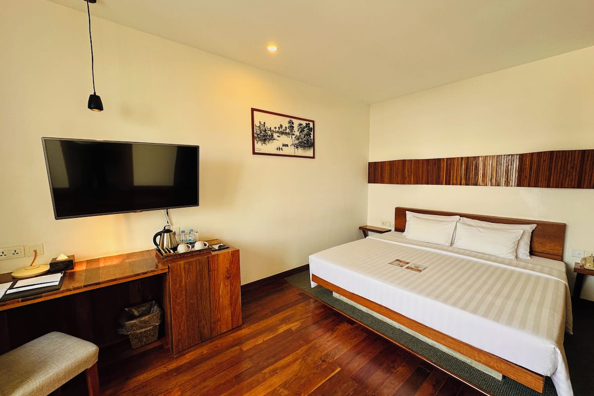 Hotelkamer met een bed, een bureau met een televisie, een houten hoofdeinde en een aan de muur hangend schilderij.
