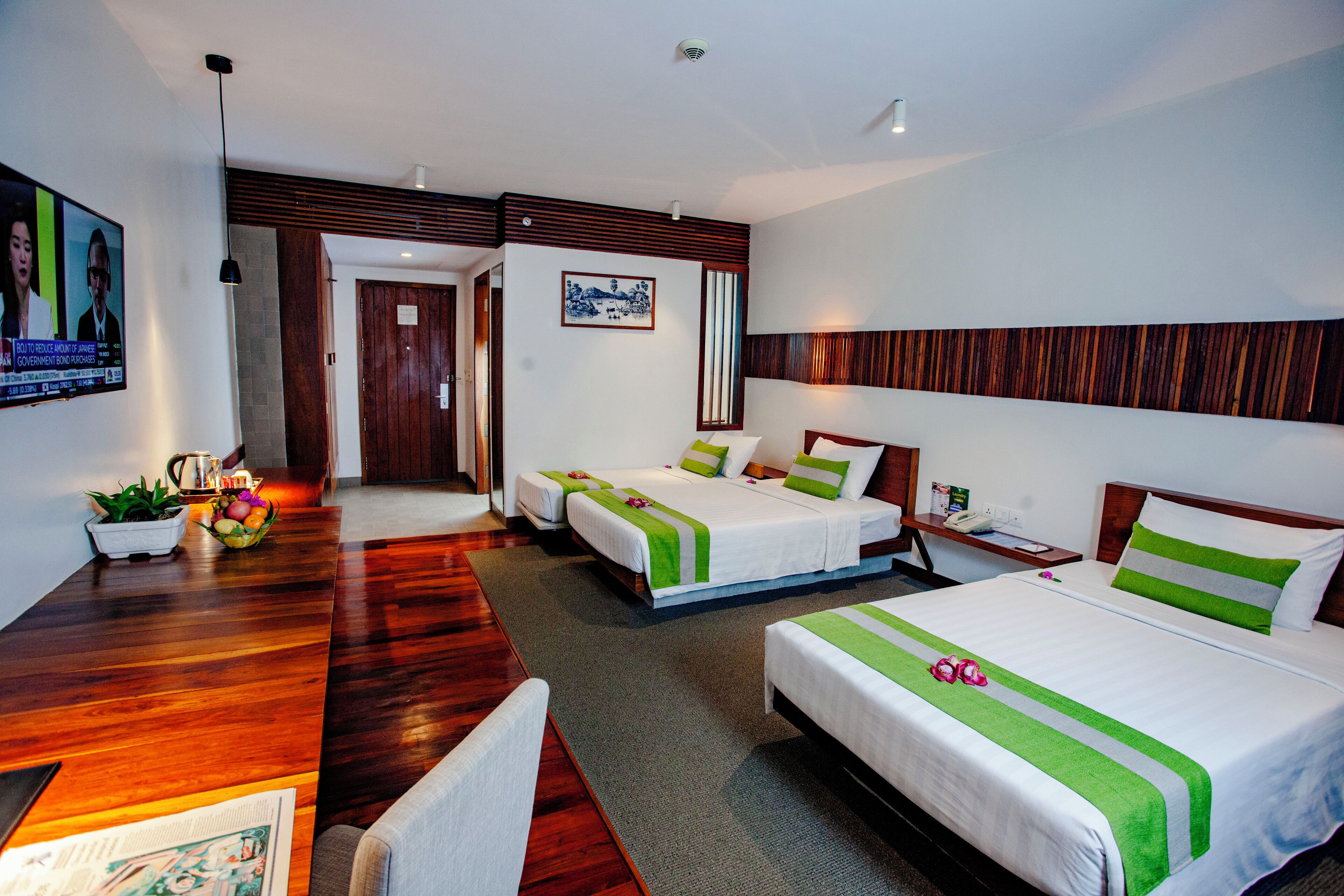 A hotel room with two beds, a desk, and a chair. There is a television on the wall and a plant on the desk.