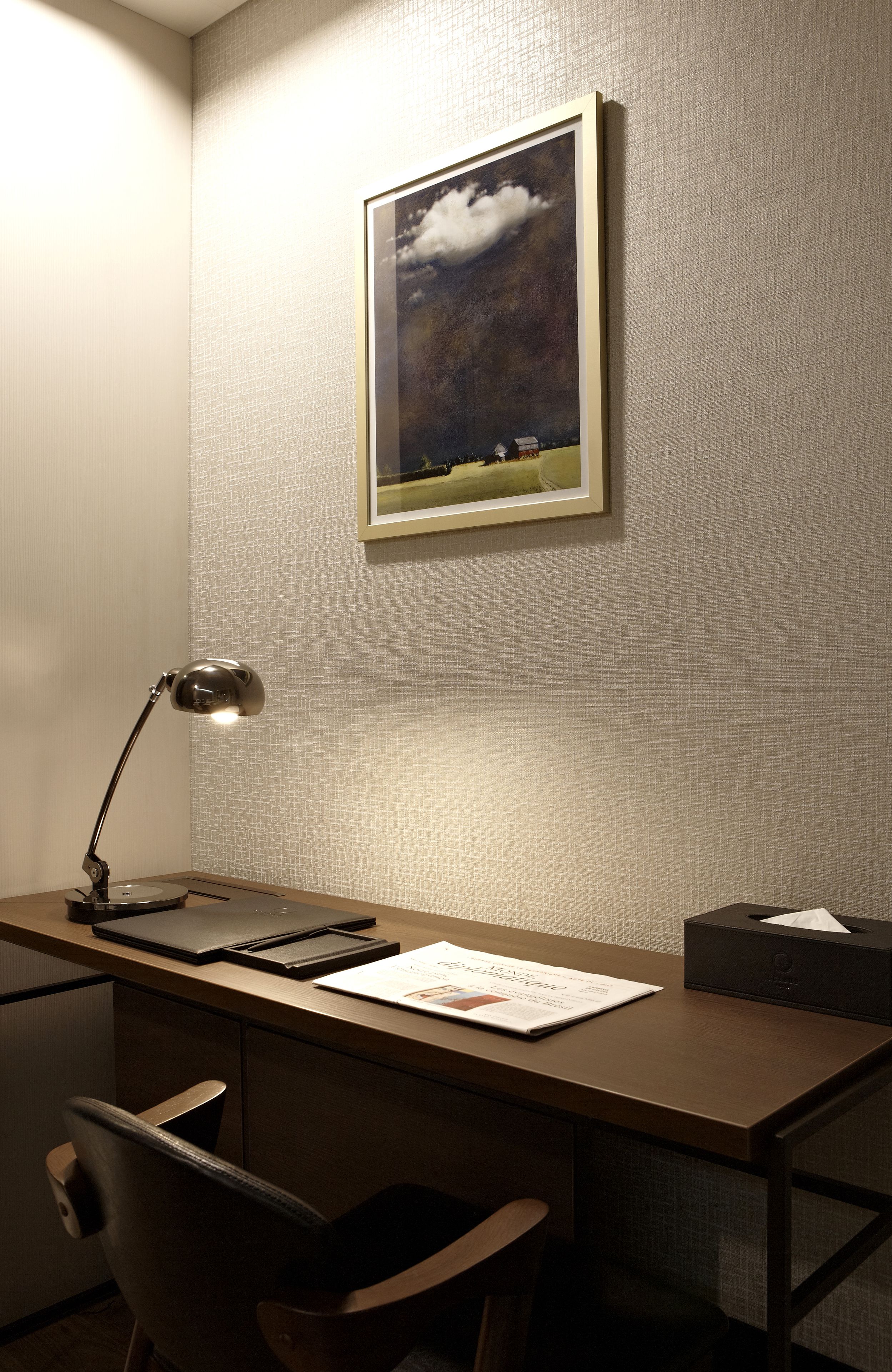 A desk with a lamp, a chair, a framed picture on the wall, and a tissue box.