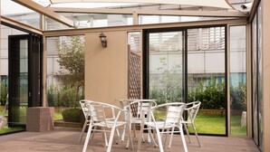 Un patio cubierto con cerramiento de vidrio, que incluye una mesa, sillas, un farol y vistas a un jardín.