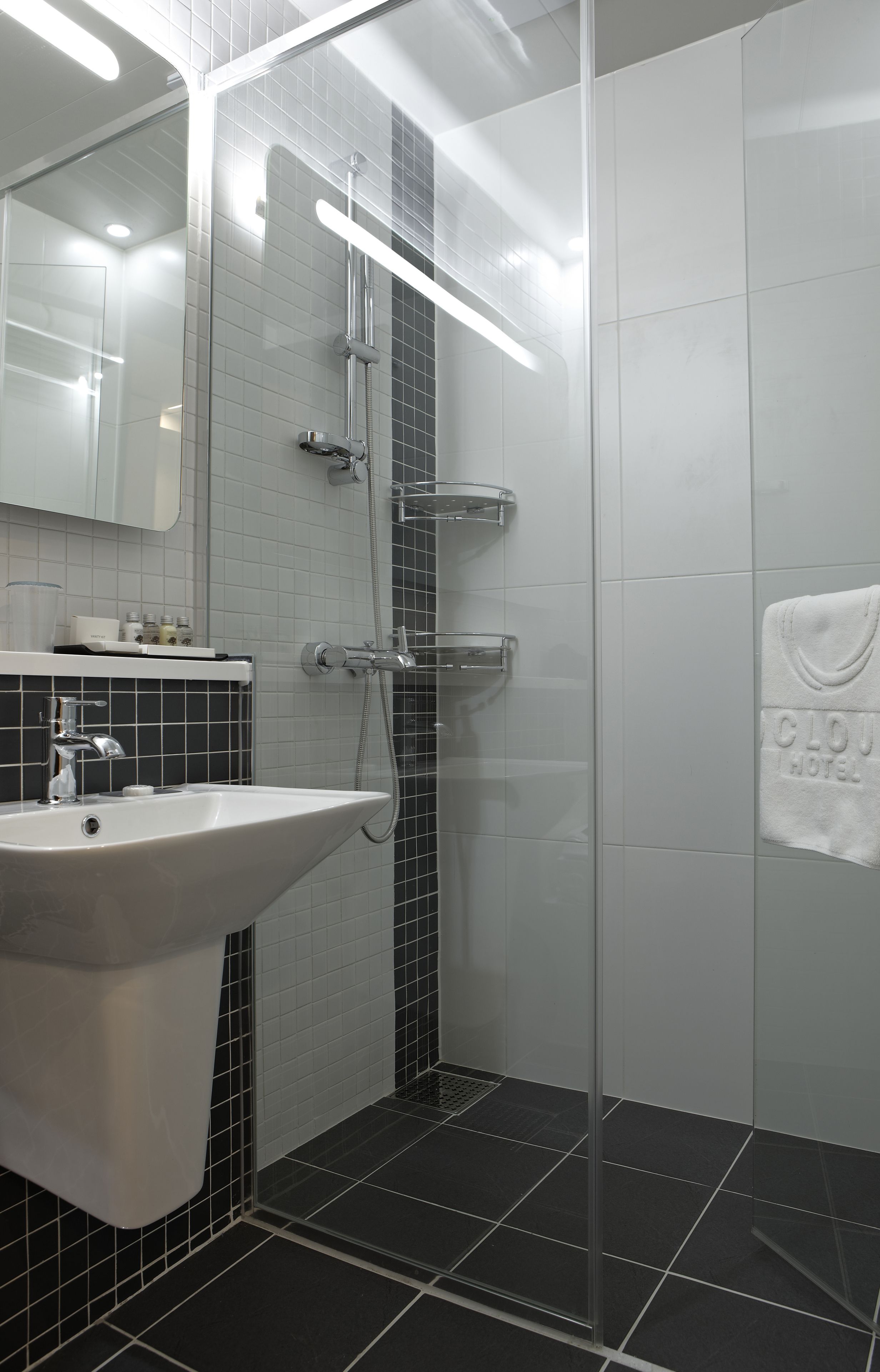 A modern bathroom with a glass-enclosed shower, a white sink, and a towel hanging on the wall.