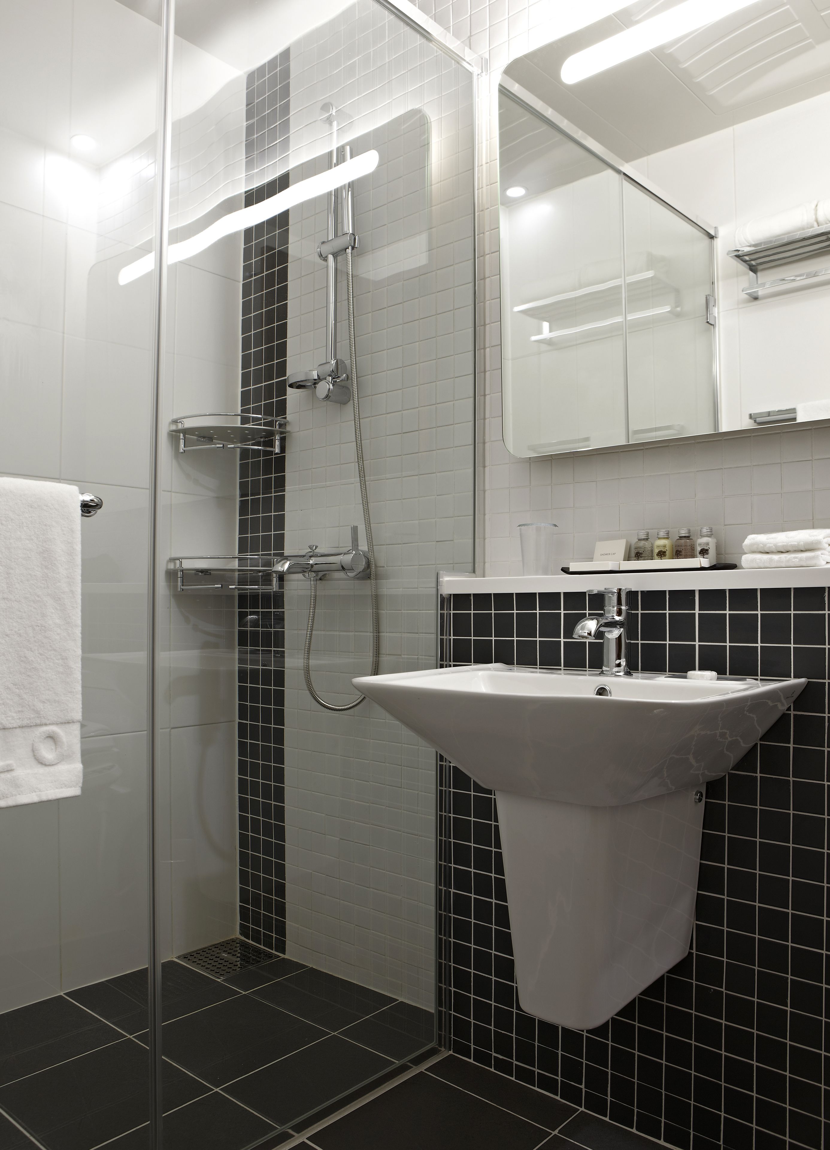 A modern bathroom with a glass shower enclosure, a white sink, and a black tiled backsplash.