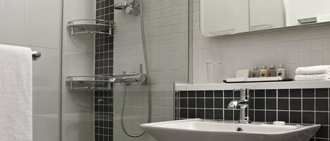 A modern bathroom with a glass shower enclosure, a white sink, and a black tiled backsplash.