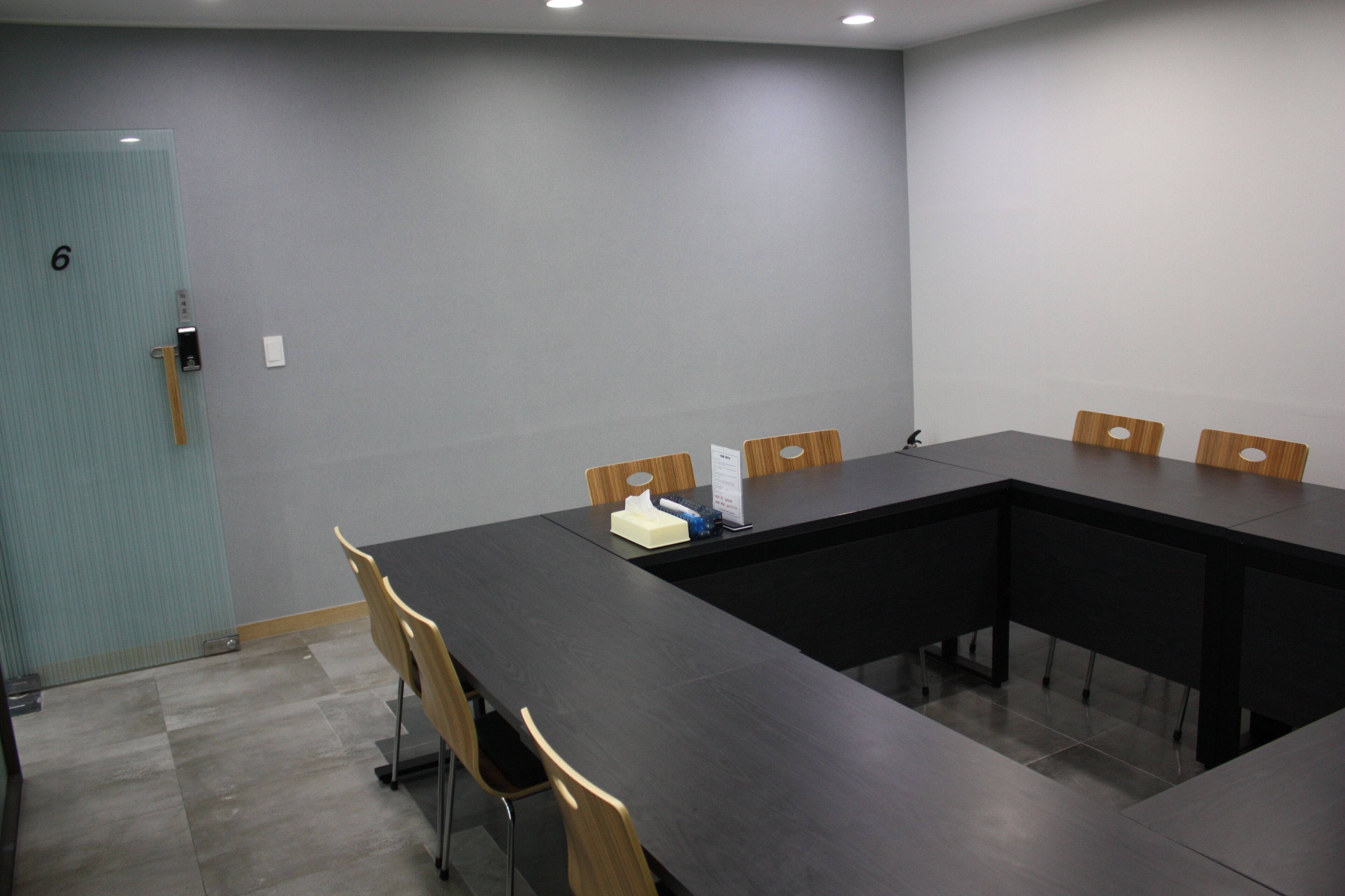 A conference room with a long table, six chairs, and a door marked with the number 6.