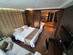 A modern hotel room with a large bed, a sofa, a TV, and a kitchen area visible through an open door. - Ocloud Hotel Gangnam (Seoul)