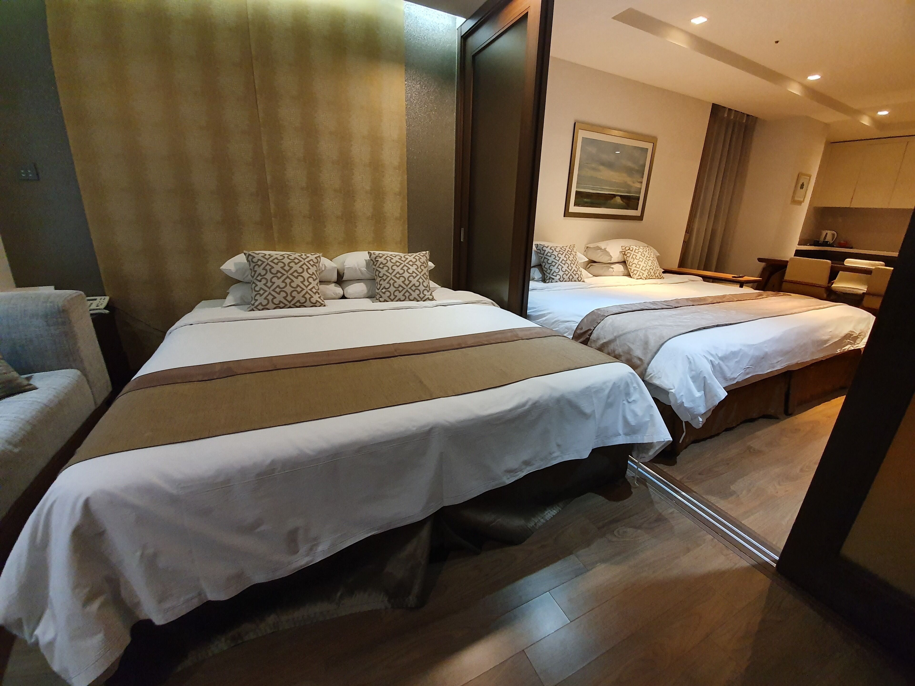 A hotel room with two beds, a large mirror, a wooden floor, and a painting on the wall.