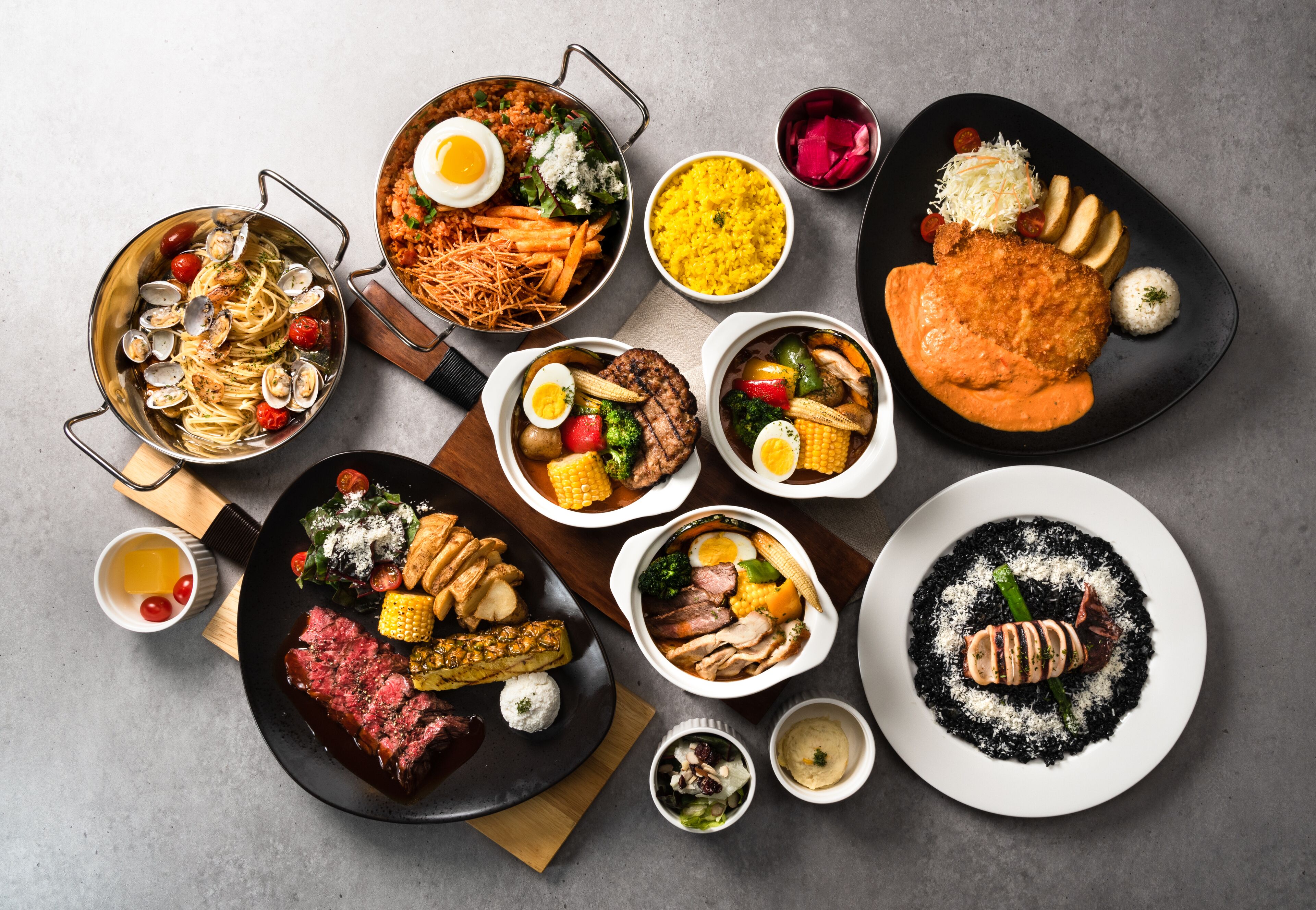 A variety of dishes including pasta, steak, and rice, arranged on a table.