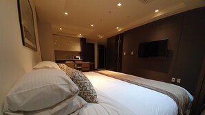 Una habitación de hotel moderna con una cama grande, un televisor de pantalla plana en la pared y una pequeña kitchenette al fondo.
