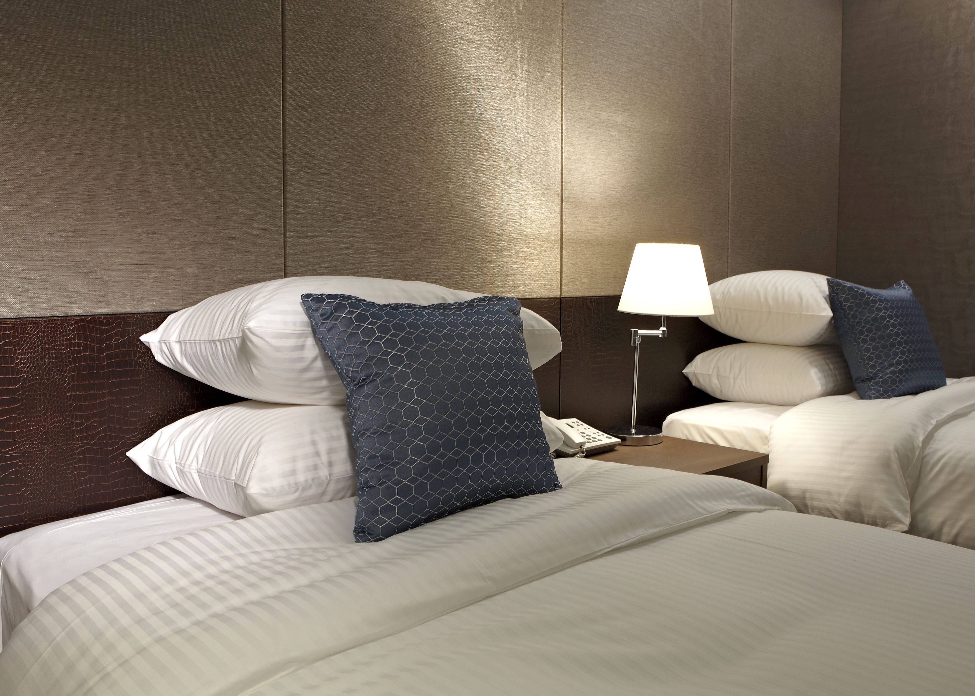 A hotel room with two beds, a nightstand with a lamp, and a telephone.