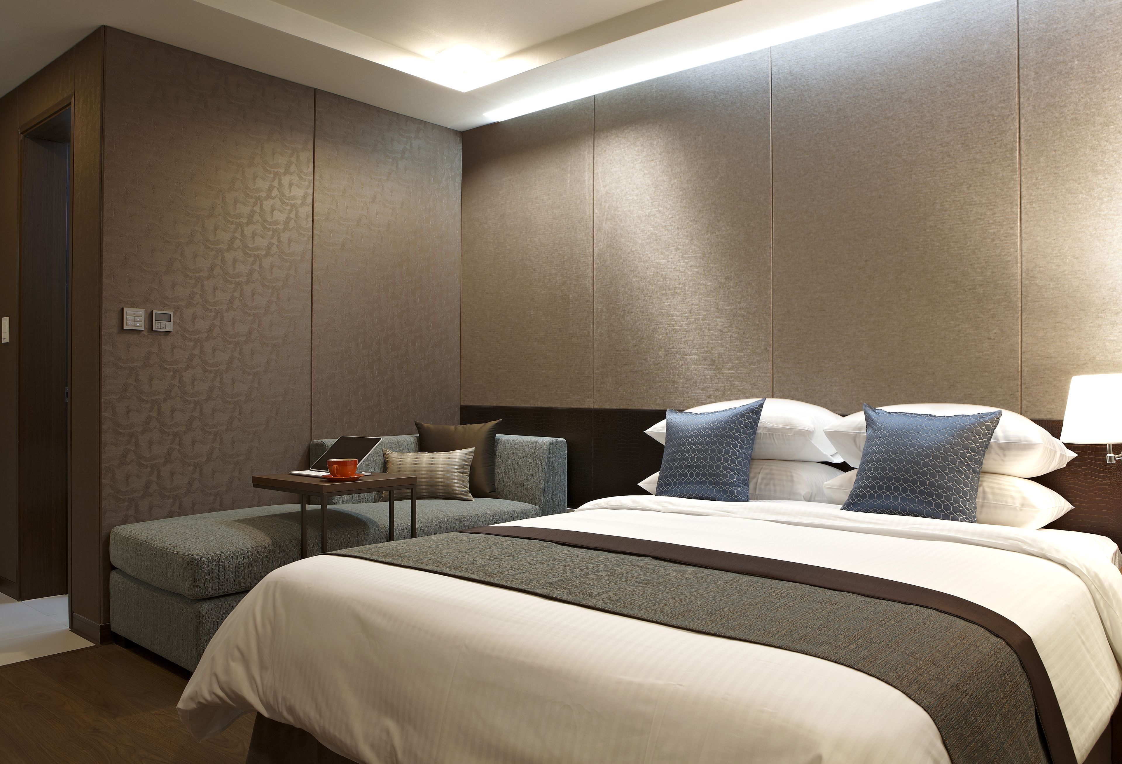 A hotel room with a bed, a small table with a laptop, a chair, and a sofa.