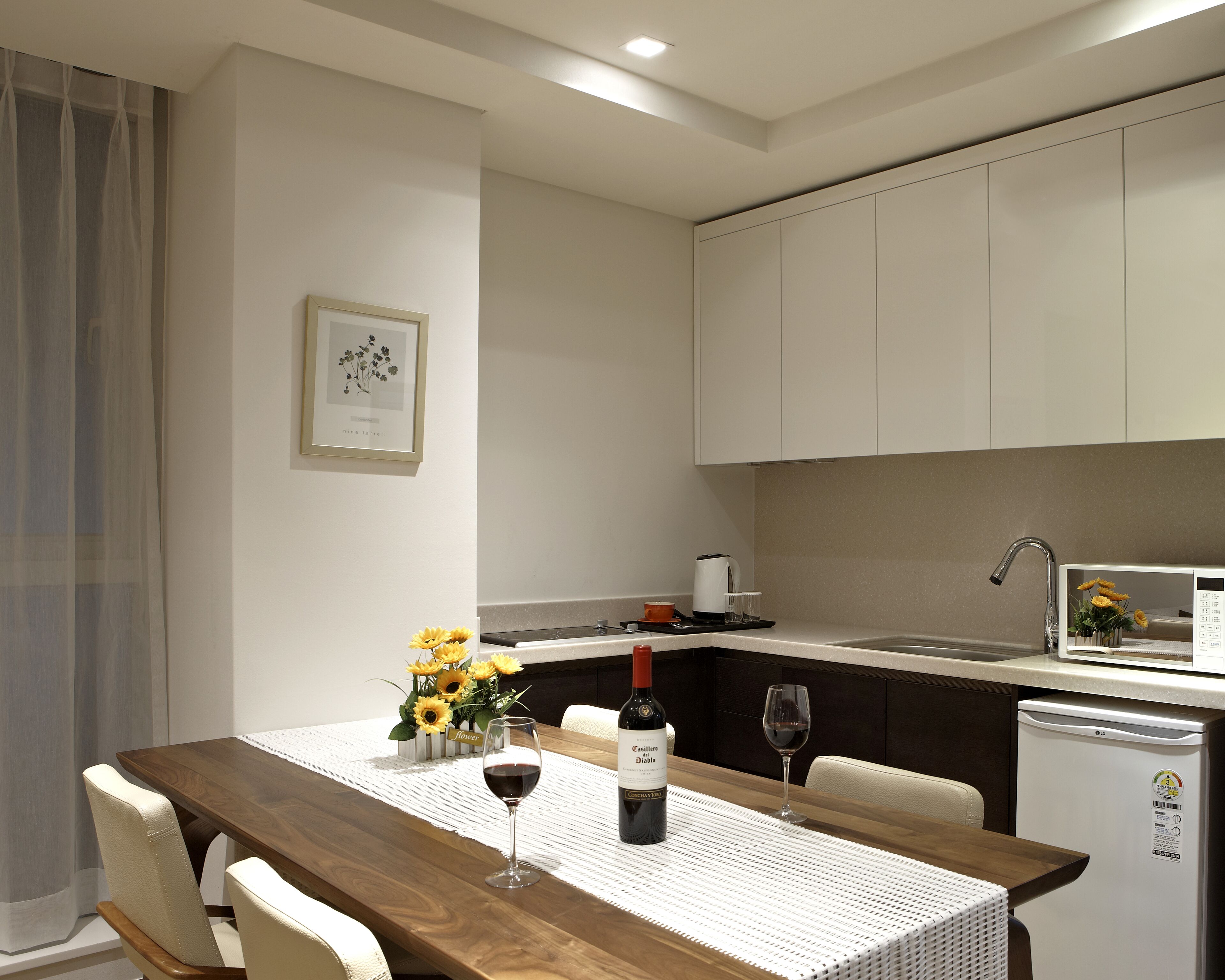 A modern kitchen with white cabinets, a wooden dining table, and a refrigerator.