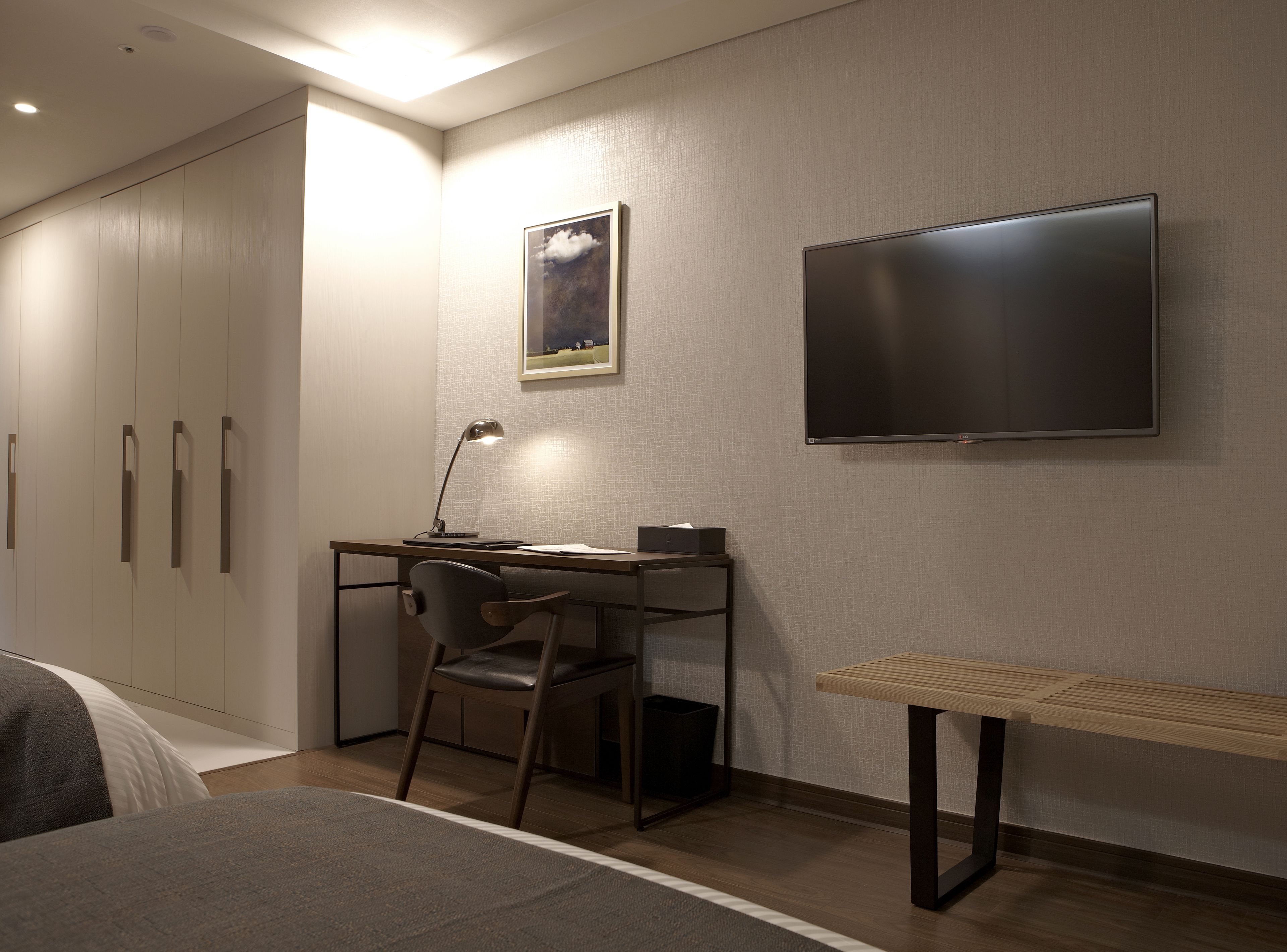 Habitació d'hotel moderna amb un llit, una taula de treball amb una cadira, una televisió i un quadre al mur.