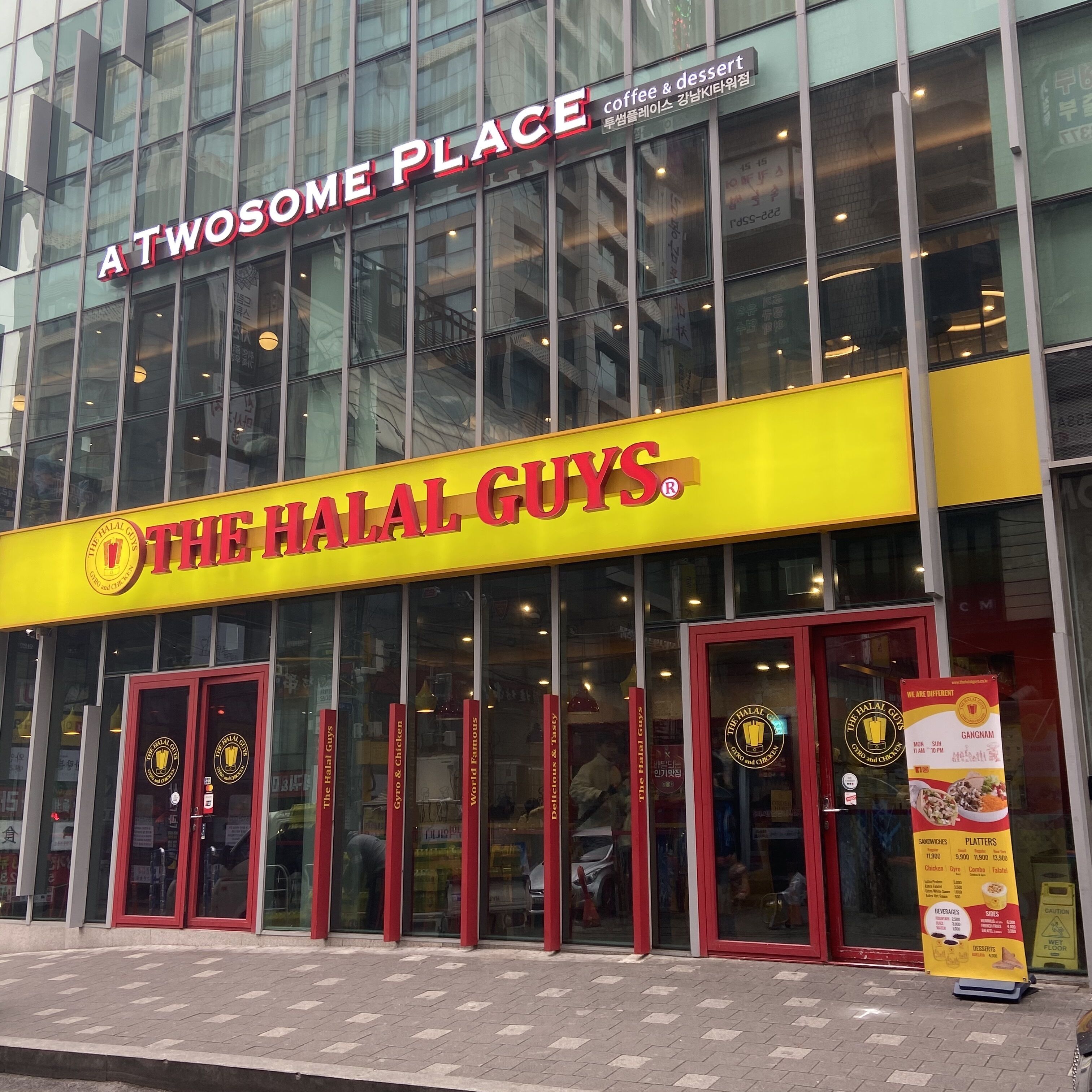 Un edifici amb un cartell groc que diu “The Halal Guys” i un altre cartell a dalt que diu “Atwesome Place”.