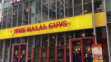 Un edifici amb un cartell groc que diu “The Halal Guys” i un altre cartell a dalt que diu “Atwesome Place”.