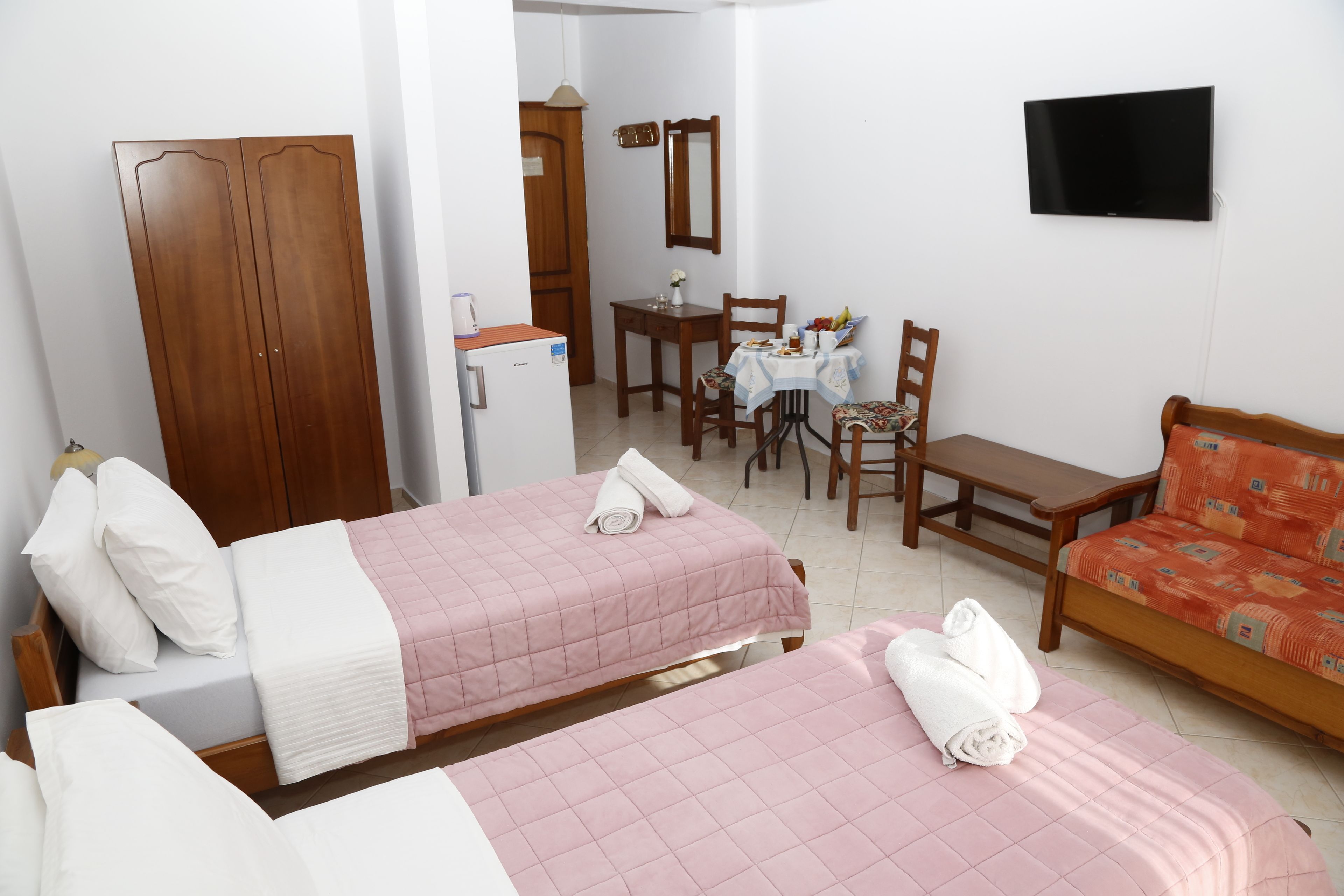 A hotel room with two beds, a desk, a chair, a television, and a wardrobe.