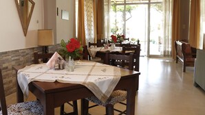 A dining area with wooden tables and chairs, a vase with red flowers, and a mirror on the wall. - Athina Rooms (Rethymno)