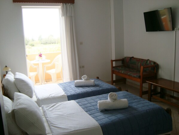 A hotel room with two beds, a TV, a sofa, and a balcony with chairs. - Athina Rooms (Rethymno)
