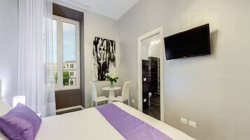 A hotel room with a bed, a TV, a small table with chairs, and a window with curtains.