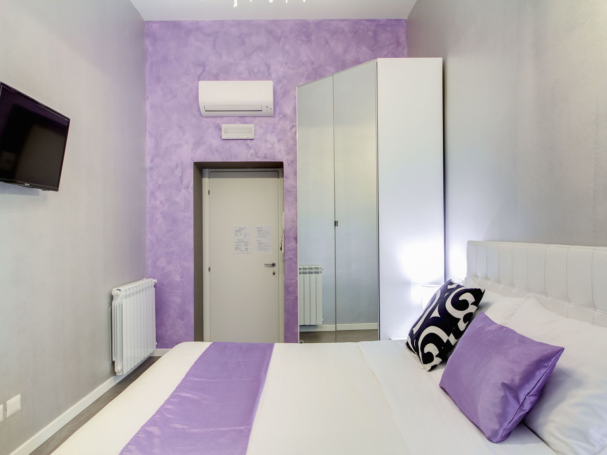 A bedroom with a bed, a TV, a wardrobe, and a door.