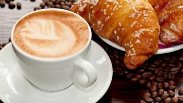 A cup of coffee with latte art on a saucer, a croissant, and scattered coffee beans.
