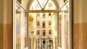 Vista desde un balcón con puerta de cristal, que da a un patio interior con una escalera central, rodeado de edificios con ventanas y balcones arqueados.