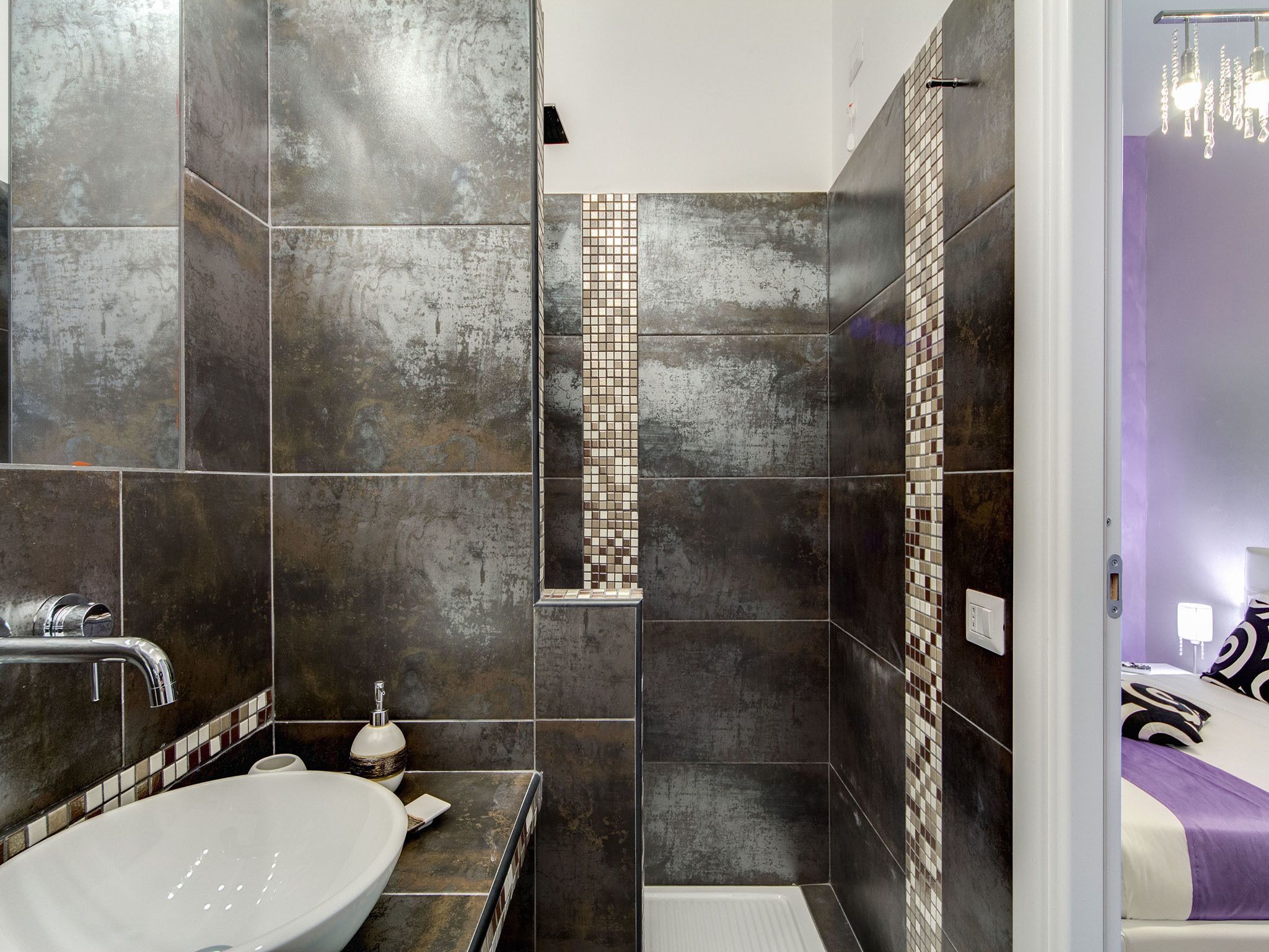 A modern bathroom with a large sink, dark tiles, and a shower area.