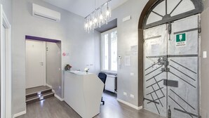 Zona de recepción con mostrador, candelabro, una puerta con señalización de salida de emergencia y una escalera que conduce a otra habitación.