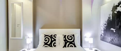 A bedroom with a large bed, two bedside tables with lamps, a mirror, and a wall with a black and white abstract design.