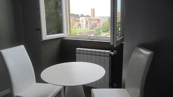 A room with a round table and two white chairs, a window with a view of buildings, and a radiator.