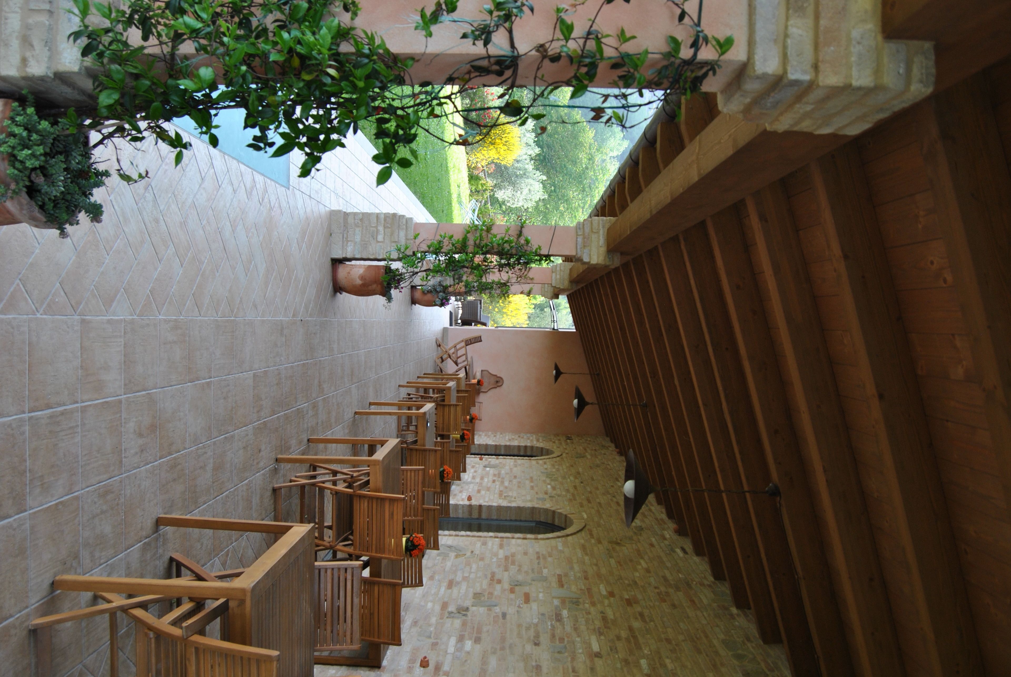 Une rangée de bancs en bois, placée sous un mur recouvert de carreaux et agrémentée de plantes suspendues, mène à une clôture en bois.