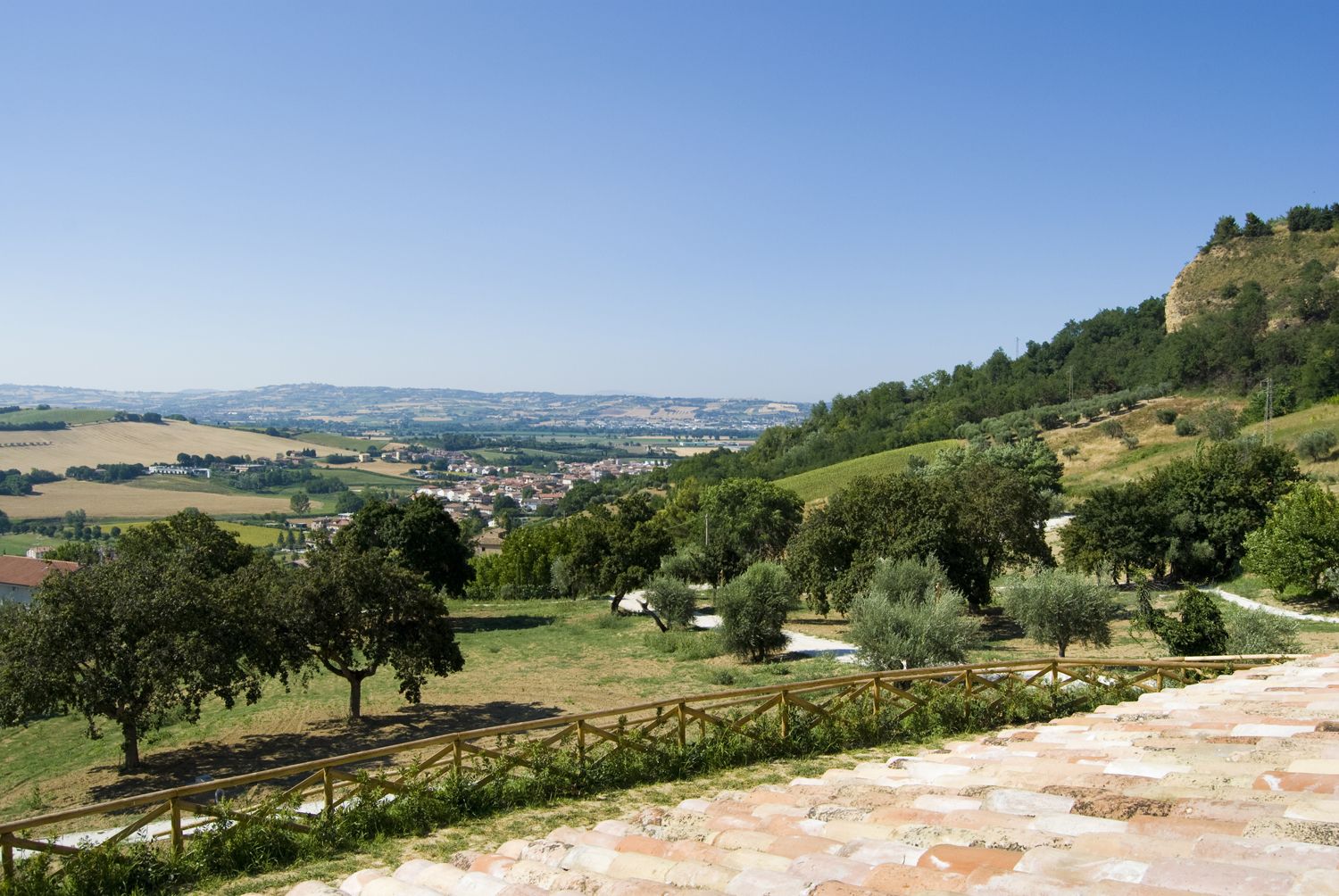 A scenic view of a town nestled in a valley with a stone pathway leading up to a wooden fence.