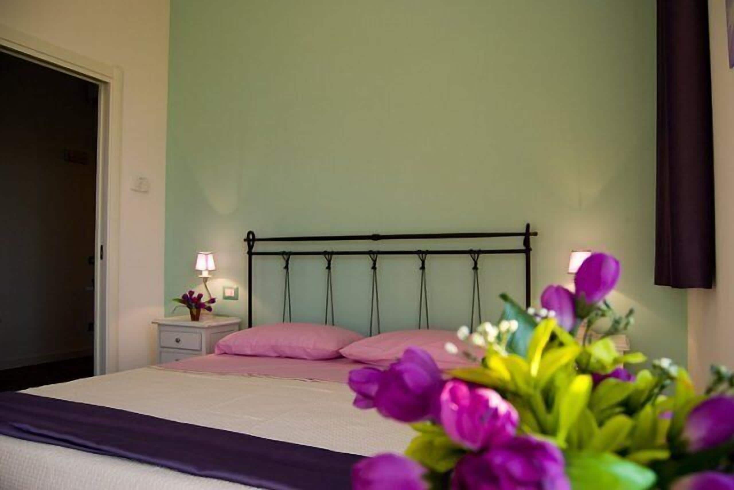A bed with a headboard, a nightstand with a lamp, and a vase of flowers.