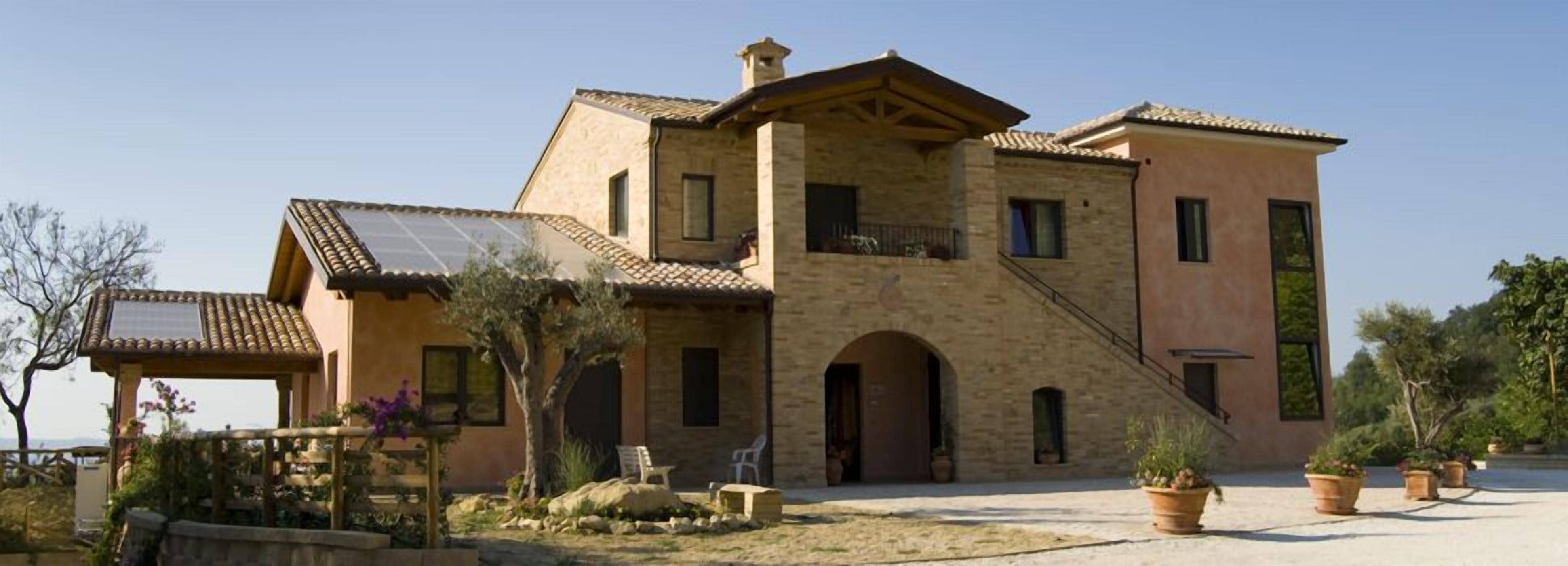 A large, two-story house with a stone facade, a balcony, and a small garden area with potted plants.