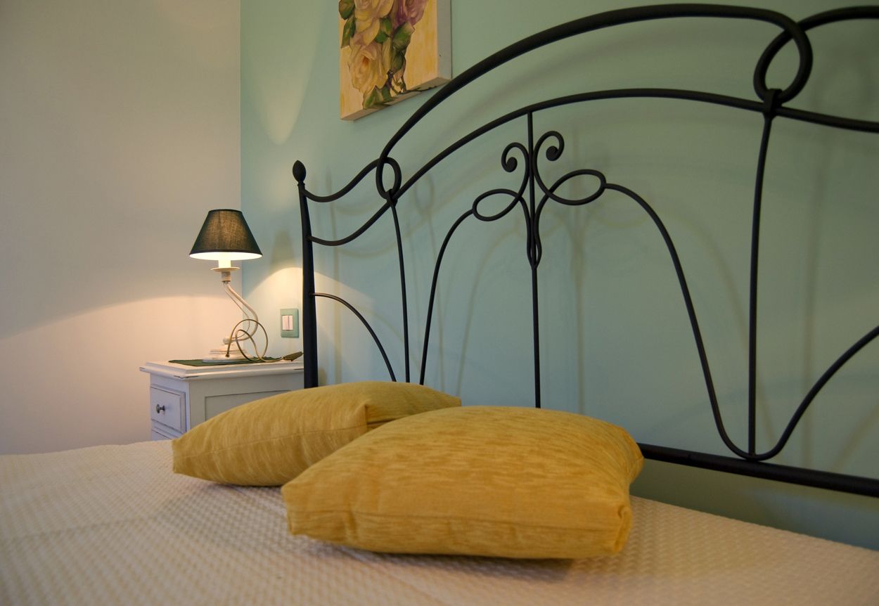 Una cama con dos almohadas amarillas, una mesita de noche con una lámpara y una pared con un cuadro.