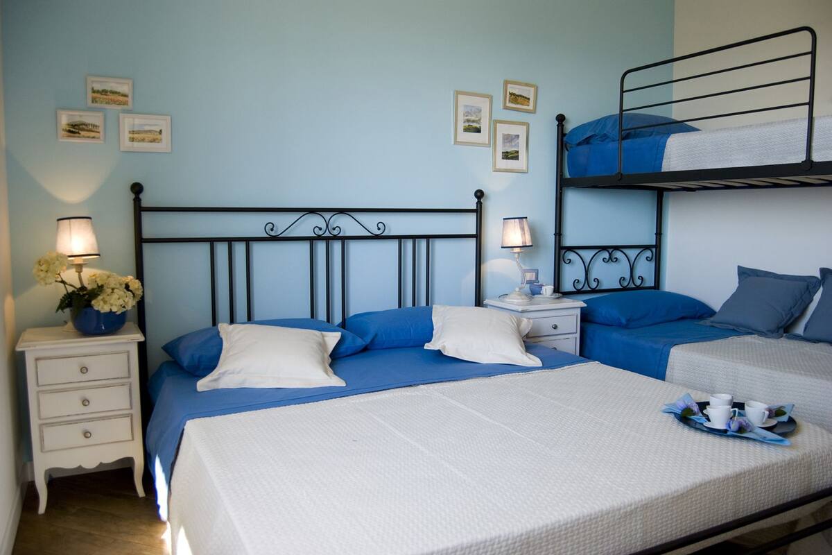 Une chambre avec un lit superposé, un lit simple, des tables de chevet avec des lampes et une commode.