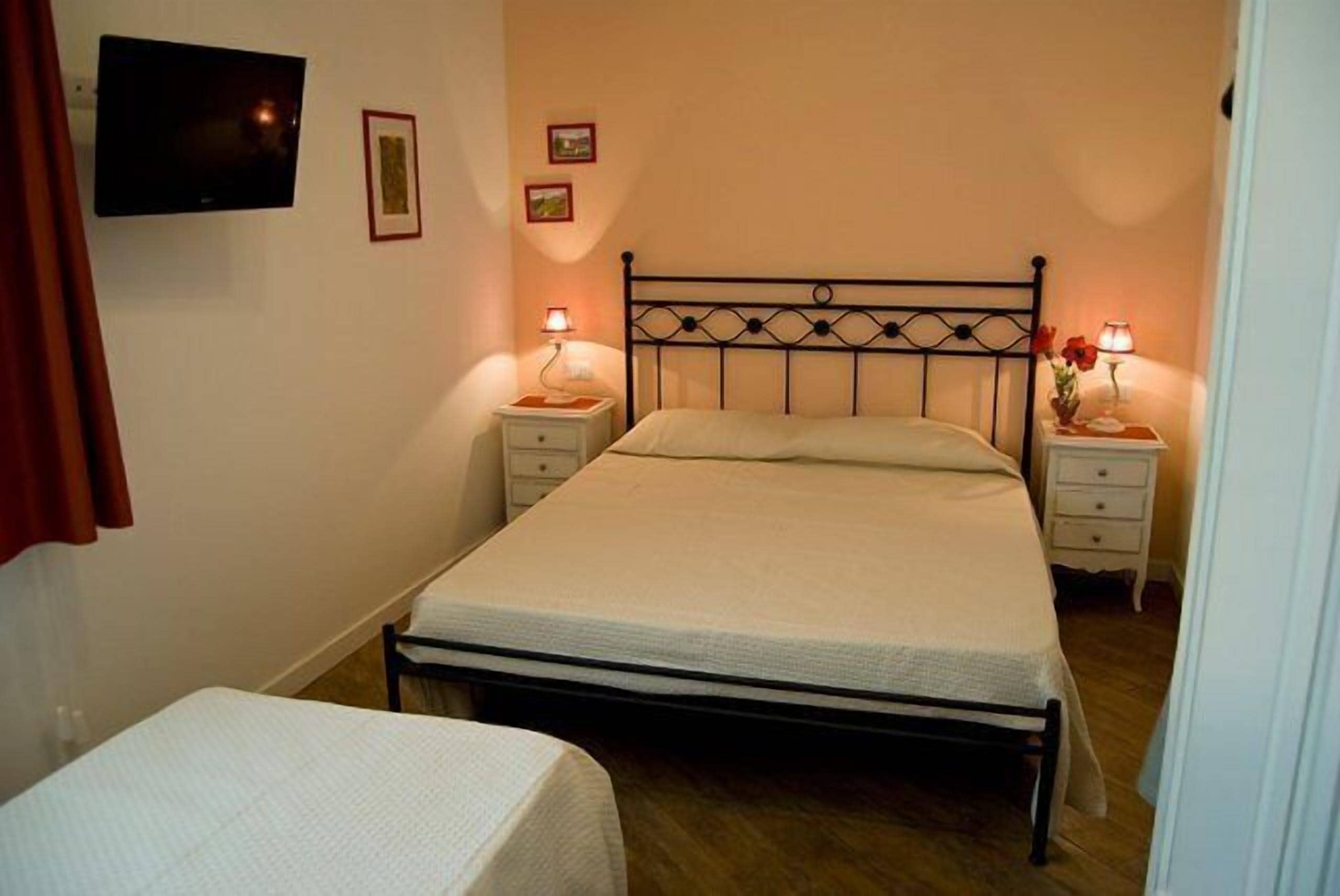 Een slaapkamer met een bed, twee nachtkastjes, een aan de muur bevestigde televisie en een kleine tafel met een bloemenvaas.