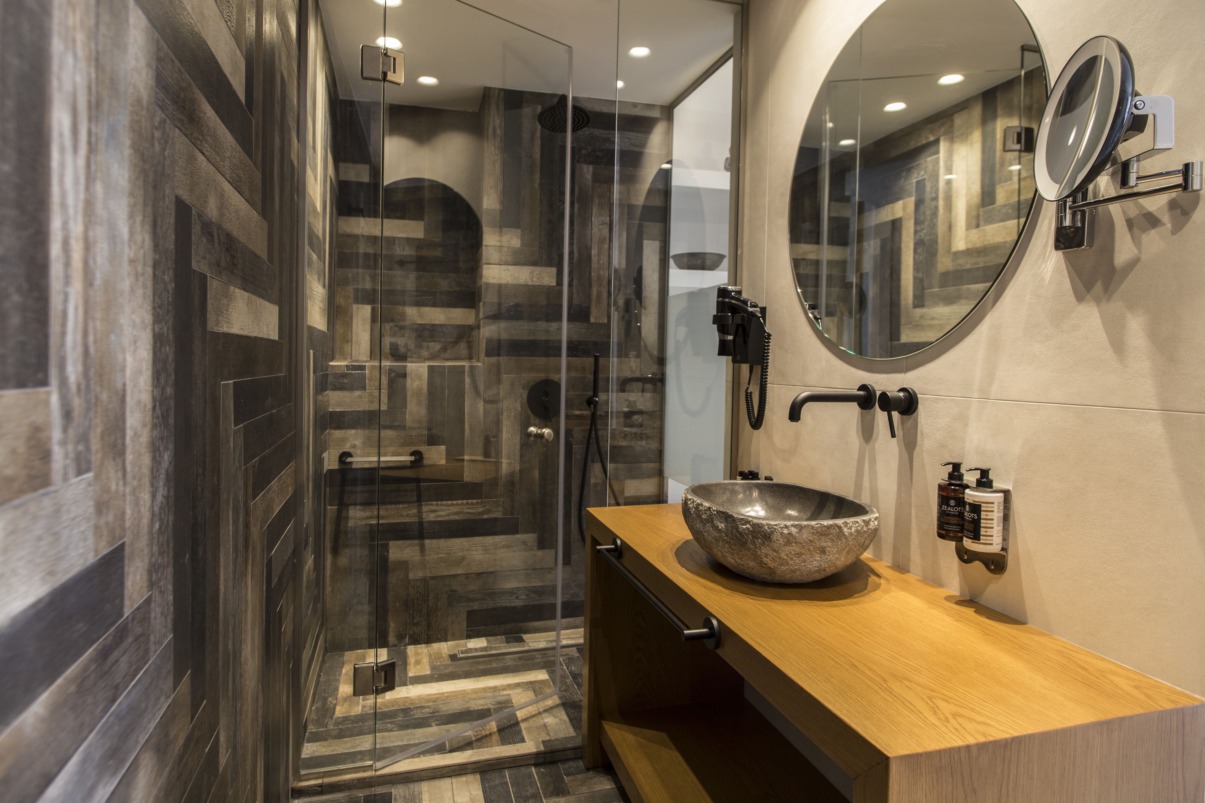 A modern bathroom with a glass-enclosed shower, a wooden vanity with a large basin, and a wall-mounted mirror.