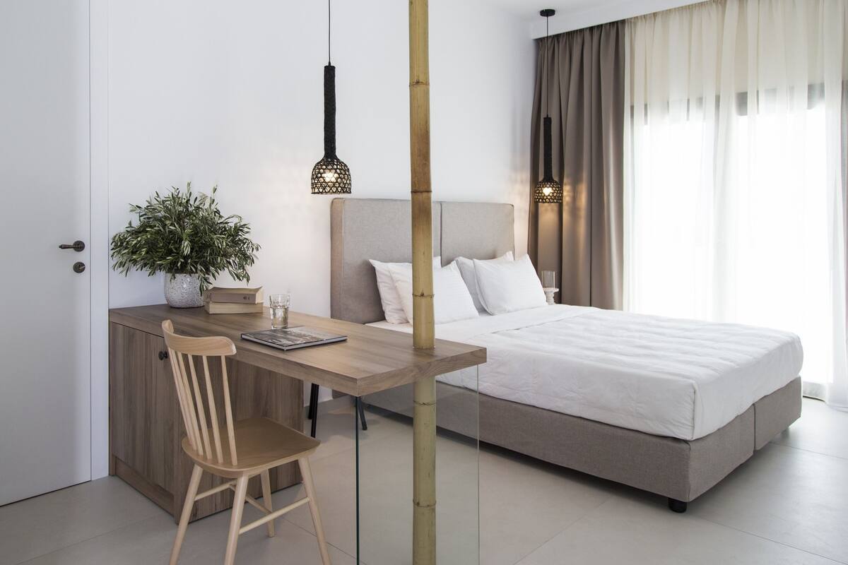 A modern bedroom with a bed, bedside table, chair, and a desk with a chair.