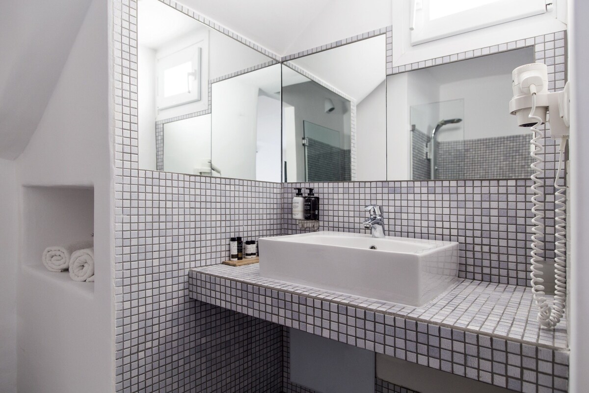 A modern bathroom with a large mirror, a white sink, and a towel rack.