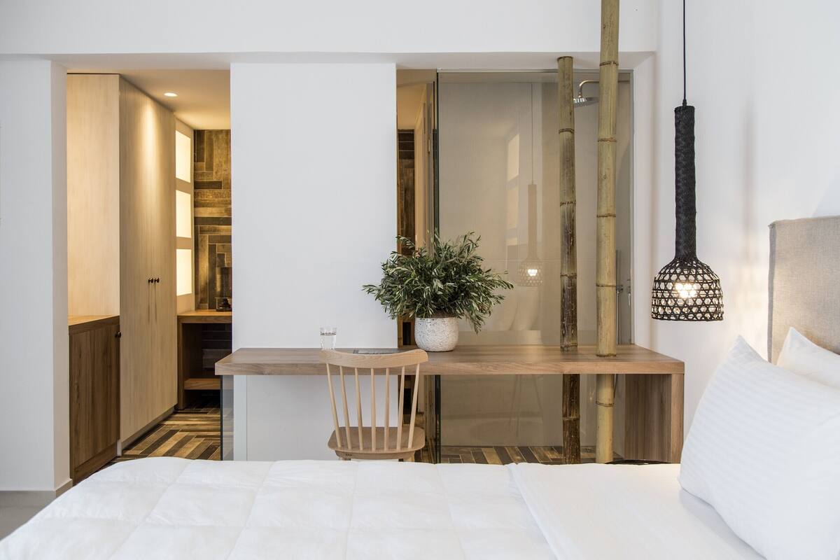 A modern bedroom with a bed, a wooden desk, a chair, a potted plant, and a hanging light fixture.
