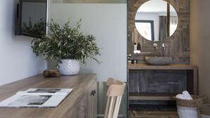 Un baño moderno con tocador de madera, una planta en maceta, un espejo y un lavabo con encimera de piedra.