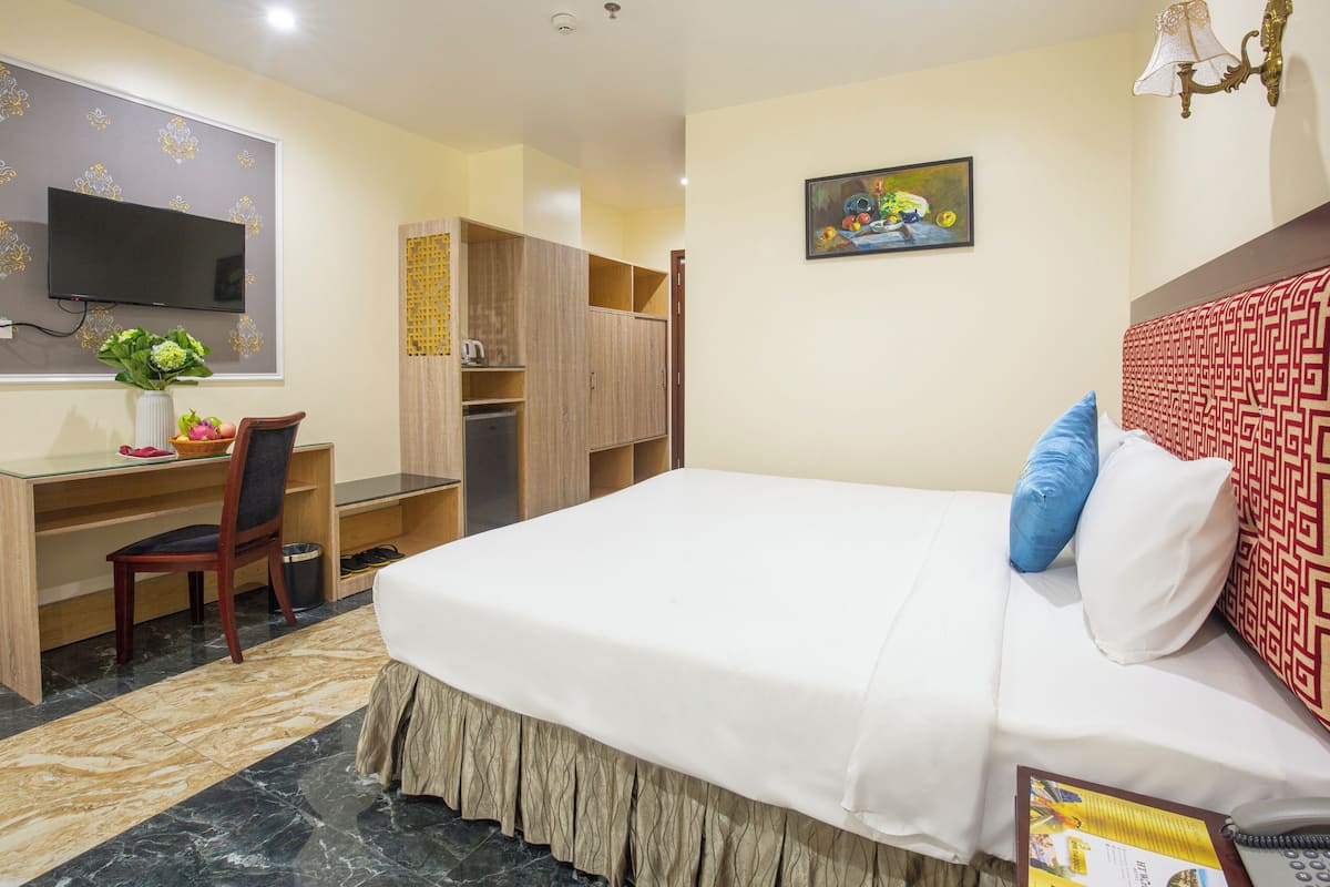 A hotel room with a bed, desk, chair, wardrobe, and a television on the wall.